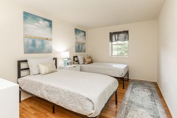 two beds in a room with a hardwood floor and two paintings on the wall